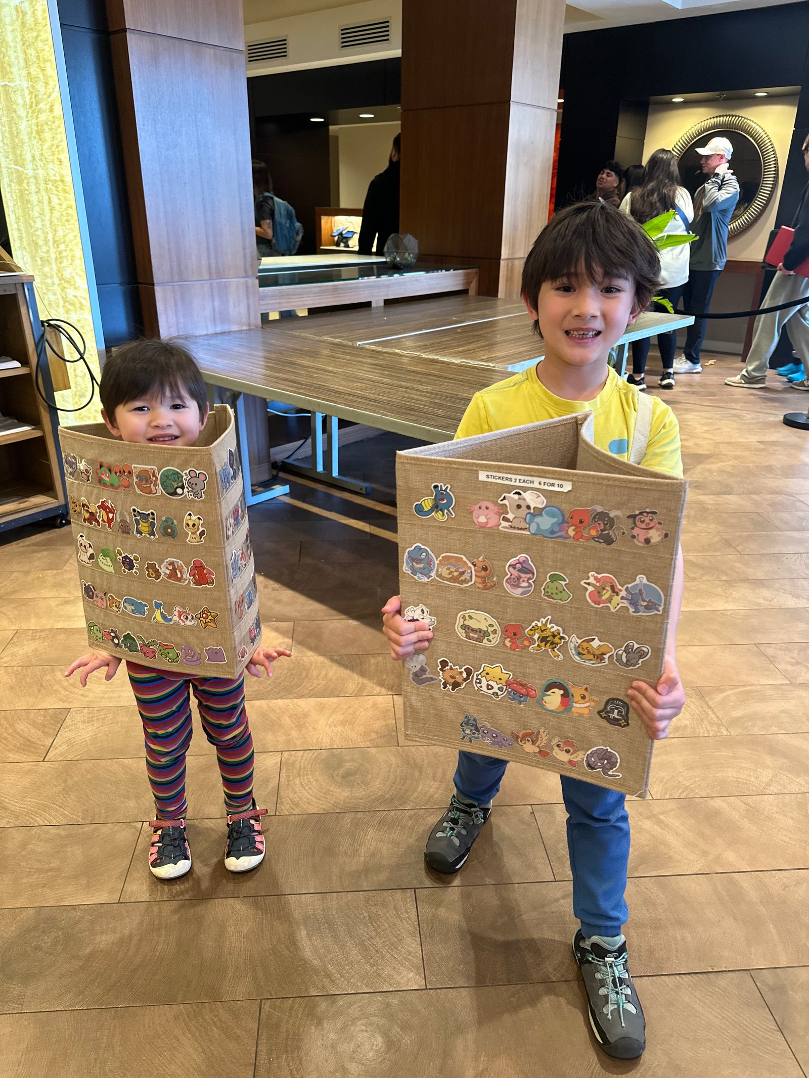 Fionn and his sister at a convention, each holding a handmade cardboard display board covered in Pokémon stickers for sale.